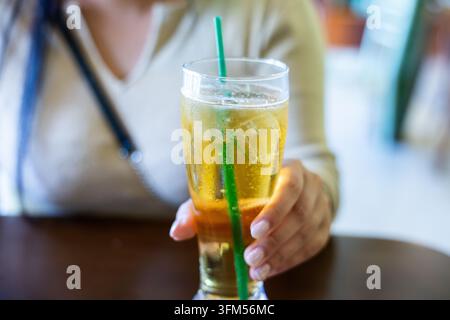 Una donna che tiene una bevanda al limone ghiacciata con cannuccia in un caffè, bevanda rinfrescante che brilla su uno sfondo sfocato Foto Stock