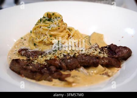 Pasta cremosa ricoperta da una fetta di bistecca di manzo tenera grigliata su un piatto bianco Foto Stock
