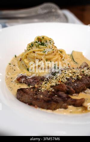 Pasta cremosa ricoperta da una fetta di bistecca di manzo tenera grigliata su un piatto bianco Foto Stock