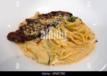 Pasta cremosa ricoperta da una fetta di bistecca di manzo tenera grigliata su un piatto bianco Foto Stock