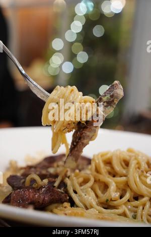 Pasta cremosa ricoperta da una fetta di bistecca di manzo tenera grigliata su un piatto bianco Foto Stock