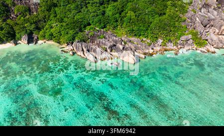 Formazioni granitiche distintive costeggiano una turchese costa tropicale con acqua limpida. Seychelles, La Digue. Foto Stock
