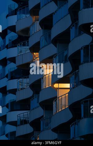 Facciata di un moderno edificio di appartamenti di lusso con balconi curvi a forma di onda illuminati al crepuscolo Foto Stock