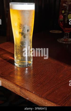 Un bicchiere freddo di lager su un tavolo di legno alla forte luce trasversale. Foto Stock