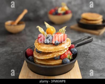 Pancake fatto in casa a strati con mirtilli freschi, lamponi e menta, servito in una piccola padella Foto Stock