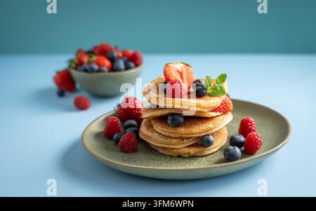 Pancake fatto in casa a strati con mirtilli freschi, lamponi e menta, servito su un piatto con spazio libero blu Foto Stock