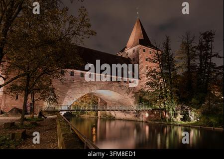 Vista notturna del ponte Kettensteg a Norimberga con architettura in arenaria illuminata, acqua calma e riflessi Foto Stock