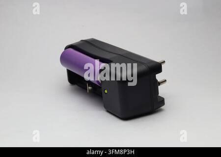 Caricatore portatile per batteria agli ioni di litio con cella inserita e indicatore LED acceso su sfondo bianco Foto Stock