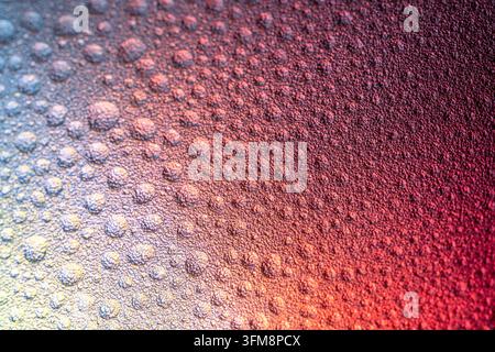 Primo piano di goccioline d'acqua su una superficie di plastica ruvida, che formano uno sfondo astratto con una vivace sfumatura di rosso e blu Foto Stock