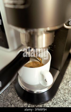 Macchina per l'espresso che versa caffè caldo in una tazza di ceramica bianca su un bancone della cucina Foto Stock