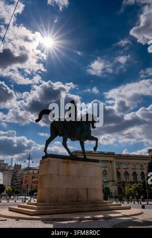 Bucarest, Romania - Settembre 2026: Silhouette dell'allegoria equestre di Carol I in Piazza della Rivoluzione catturata contro un cielo drammatico illuminato da un fascio di luce solare. Foto Stock