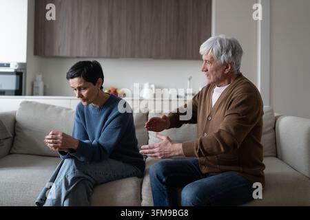 Coppia di anziani in seria discussione e incomprensione, seduti insieme sul divano del soggiorno. Foto Stock