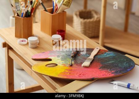 Palette di legno per artisti con pennelli e barattoli di vernice sul tavolo Foto Stock