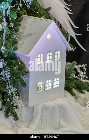 Lanterna bianca a forma di casa con finestre ad arco vicino all'albero di Natale, ornamenti festivi, colori pastello morbidi, atmosfera accogliente, design stravagante, legno caldo Foto Stock