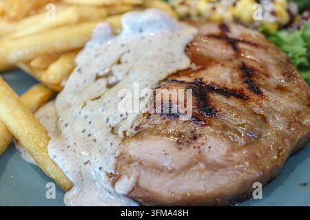 Bistecca di collo di maiale grigliata con segni di griglia e salsa ai funghi al tartufo servita con patatine fritte su un piatto blu grigio a Bangkok, Thailandia Foto Stock