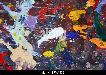 Residui di vernice multicolor stratificati su un tavolo di attività artistica in legno scuro in Thailandia, primo piano texture astratta con venatura visibile e segni scheggiati. Foto Stock