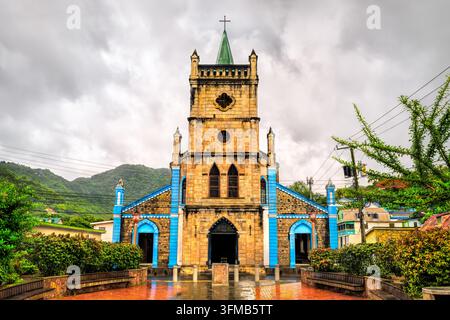 Facciata della Chiesa di Nostra Signora dell'Assunzione nella piazza del paese di Soufriere, Santa Lucia, circondata da rigogliose colline tropicali sotto un cielo nuvoloso. Foto Stock