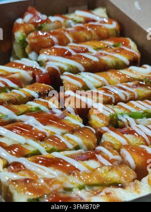 Una deliziosa assortimento di rotoli di sushi guarniti con salse saporite in una scatola da asporto Foto Stock
