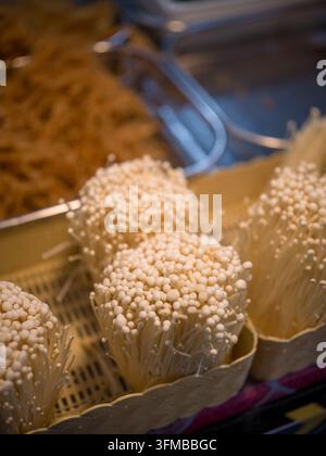 Funghi enoki freschi (Flammulina velutipes) in bicchieri di carta a una bancarella del mercato alimentare asiatico in Thailandia. Ingrediente popolare nella cucina asiatica. Foto Stock