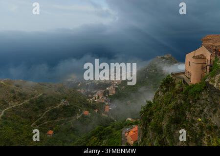 Panorama aereo drammatico e epico di un paese con la cima della collina, una casa, un cielo nuvoloso, raggi di sole e la terra sottostante lungo il mare Foto Stock