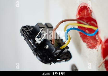Prima di una presa elettrica collegata a fili colorati nel muro. Presa appesa al muro durante l'installazione. Cablaggio elettrico, riparazione e ristrutturazione Foto Stock