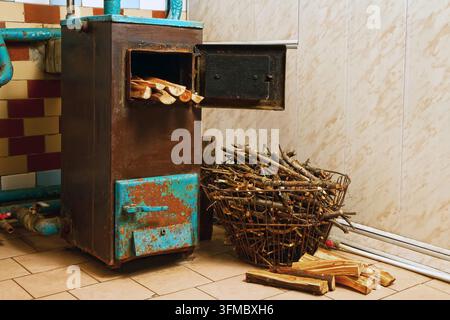 Un vecchio fornello con riscaldamento a legna invece che a gas. Cesto di legna da ardere accanto al vecchio fornello. Foto Stock