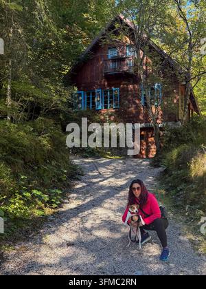 Una bella donna con lunghi capelli scuri e il suo cane Jack Russell con pelo bianco, marrone e nero, fotografati in un ambiente montano davanti a una baita Foto Stock
