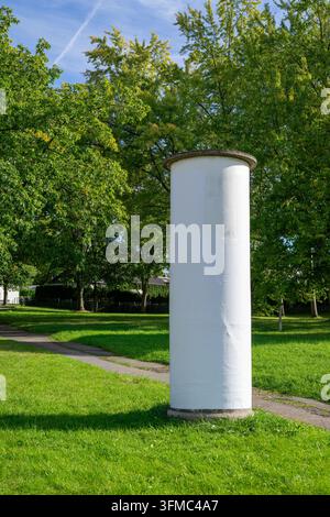 Pila pubblicitaria bianca vuota in piedi su un prato verde in un parco pubblico. Il display cilindrico vuoto offre uno spazio generoso per la pubblicità, Foto Stock