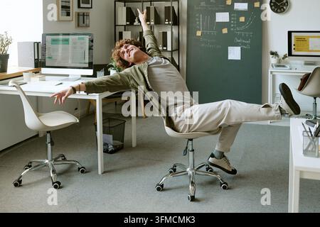 Uomo d'affari felice che balla su una sedia celebrando il successo in ufficio Foto Stock