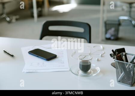Bicchiere di caffè con smartphone e documenti sulla scrivania Foto Stock