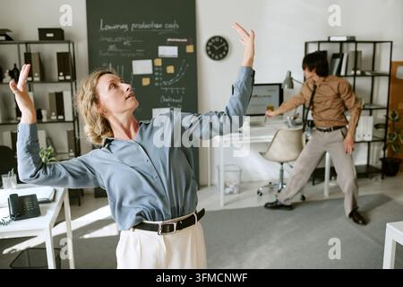 Donna di mezza età gioiosa che balla con una collega in un ufficio moderno Foto Stock