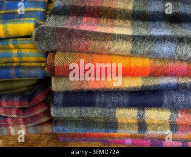 Pila di coperte di lana scozzesi tradizionali colorate e sciarpe, primo piano della trama di uno sfondo in tessuto a quadri autentico Foto Stock