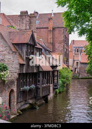 Bruges, Belgio - 23.06.2015: Edifici storici in mattoni e legno con fioriere che costeggiano un corso d'acqua panoramico in una graziosa città europea Foto Stock