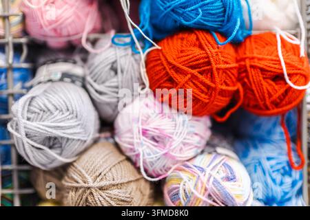 Palle di lana colorate in arancione, blu, rosa, grigio e beige riempiono una vetrina di negozio. Foto Stock