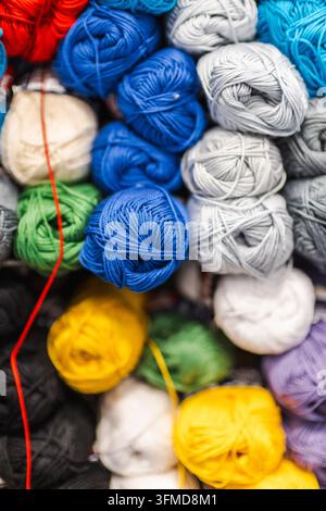 Palle di lana colorate riempiono una visualizzazione in primo piano con fibre blu, bianche, gialle, verdi, rosse, grigie e viola. Foto Stock