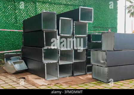 Condotti di ventilazione metallici rettangolari impilati e profili in acciaio e alluminio conservati nel cantiere edile. Foto Stock