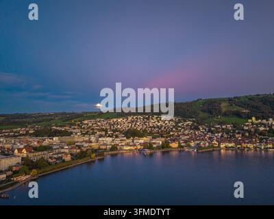 Vista drone sulla città svizzera di Zugo sul lago di Zugo con sorgere della luna nell'ora blu Foto Stock
