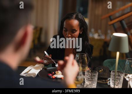 Coppia interrazziale felice che gode di un delizioso pasto di dessert gustosi in un ristorante di lusso, assaporando dolci prelibatezze. Foto Stock