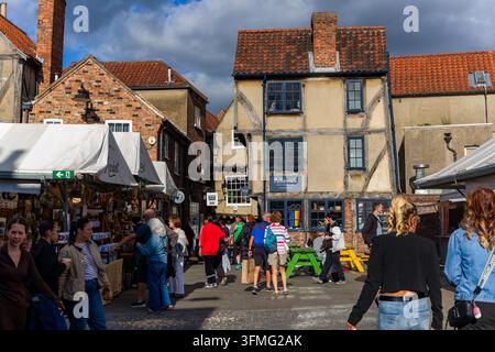 Persone che camminano attraverso il mercato di Shambles a York, in Inghilterra, sfogliando bancarelle coperte accanto ad edifici storici in legno a graticcio e sedie all'aperto Foto Stock