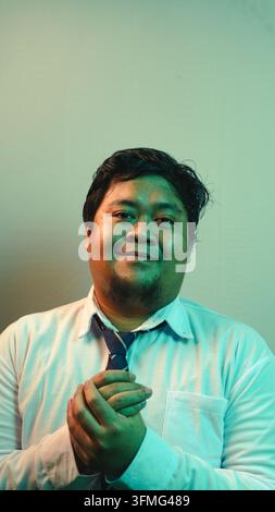 Un uomo indonesiano accessibile guarda direttamente verso lo spettatore con un sorriso gentile e le mani ben giunte. L'uomo d'affari amichevole indossa un abito formale Foto Stock