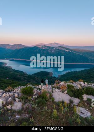 Una coppia si gode un momento sereno ammirando le viste mozzafiato del paesaggio montenegrino da Grancarevo. Le acque calme e la vegetazione lussureggiante creano uno sfondo perfetto per una fuga romantica. Foto Stock