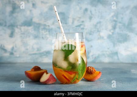 Rinfresco estivo e stile di vita sano, tè freddo alla pesca con menta fresca e cubetti di ghiaccio in un bicchiere su uno sfondo blu texture Foto Stock