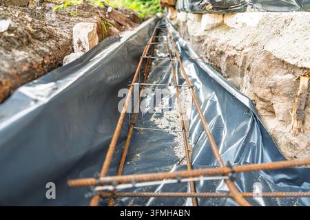 Una gabbia di rinforzo in acciaio posizionata in una trincea rivestita con pellicola di plastica nera, preparata per il getto del calcestruzzo durante la costruzione residenziale. L'immagine Foto Stock