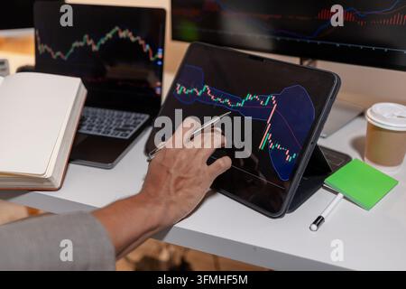 Trader professionista che analizza grafici del mercato azionario su più schermi utilizzando laptop e tablet per monitorare i movimenti dei prezzi, gli indicatori tecnici e Foto Stock