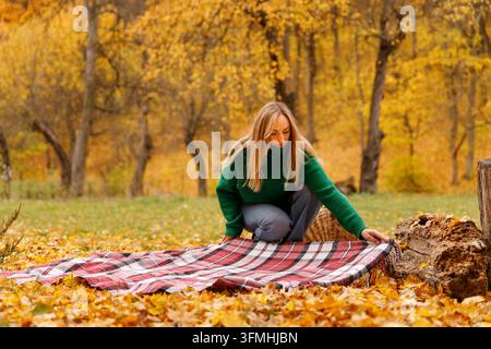 Donna che stende una coperta da picnic sulle foglie autunnali nel parco Foto Stock