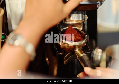 Donna che macina caffè fresco in un portafiltro nel caffè Foto Stock