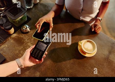 Donna nera che effettua un pagamento contactless con smartphone presso un terminale POS Foto Stock