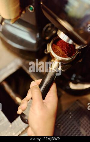 Mano di barista che tiene un portafiltro con caffè macinato in caffetteria Foto Stock