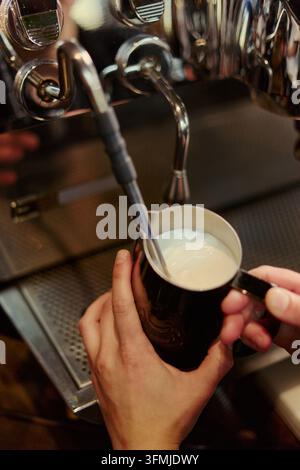 Mani del barista che consegnano latte fresco fumante con macchina per l'espresso Foto Stock