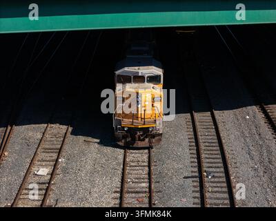 Vista aerea di una locomotiva gialla che percorre i binari sotto un ponte a Carson, California, Stati Uniti. Foto Stock